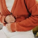 Person Suffering and Holding Belly in a House Lounge, Couch and Living Room for IBS syndrome