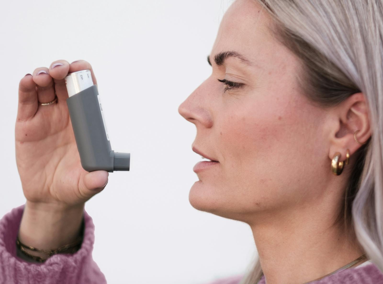Close-up of a woman using an asthma inhaler, isolated on a white background.