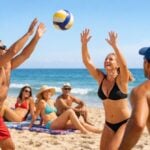 Gruppo di adulti sorridenti che giocano a beach volley e prendono il sole su una spiaggia